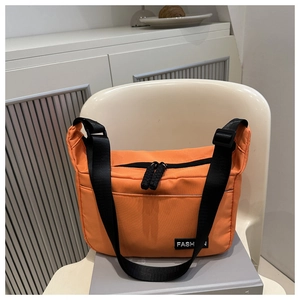 Detail of an orange nylon crossbody bag with black zippers on a white chair background