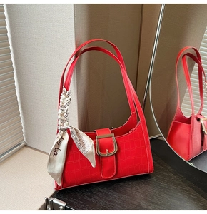 Détail du sac à bandoulière rouge motif crocodile avec boucle dorée et foulard en soie