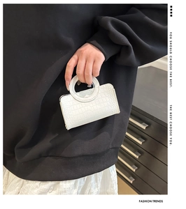 Detail of white mini handbag featuring crocodile embossed texture and circular hollow handle