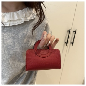 Detail of a red croc-effect mini handbag with round handle and precise stitching