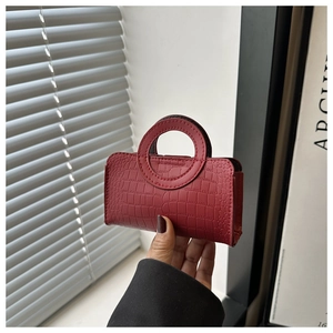 Detail view of a red mini handbag with crocodile pattern and a stylish round handle