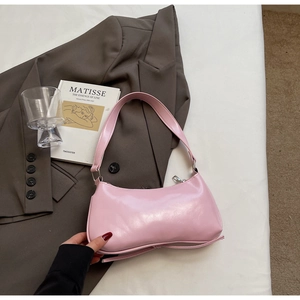 Close-up of a light pink glossy leather baguette bag placed on a chic brown blazer