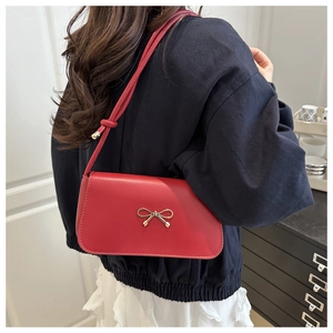 Détail du sac à épaule rouge en similicuir avec un nœud doré et un rabat plissé élégant