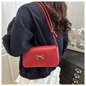 Detail of red leather underarm bag with gold bow clasp worn by model in home setting