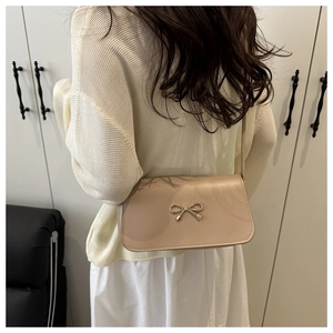 Dettaglio di una borsa a tracolla in pelle PU beige con fibbia a fiocco dorata su modella