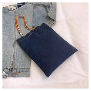 Detail of blue denim tote bag with colorful beaded handles over a denim vest background
