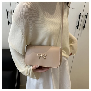 Minimalist beige crossbody bag with golden bow clasp worn by a model in a home setting