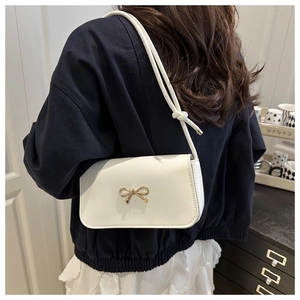 Detail of white leather shoulder bag featuring a gold bow buckle and knotted strap