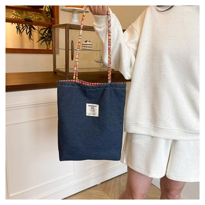 Detailed close-up of dark denim tote bag with colorful braided handles and plaid lining
