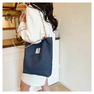 Detail of denim tote bag featuring colorful beaded straps and woven front label