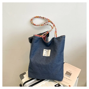 Detail of blue denim tote bag with colorful braided straps and checkered lining