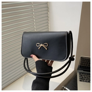 Detail of black leather flap bag with elegant gold bow buckle and slim shoulder strap
