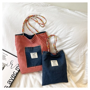 Detail of denim tote bag set featuring red plaid pockets and colorful braided handles