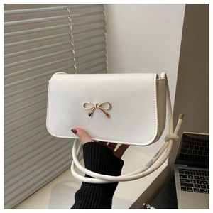 Detailed view of a white square shoulder bag with golden bow clasp and knotted strap detail