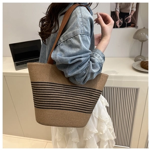 Straw tote bag with black stripes and brown strap worn by a model in a cozy room