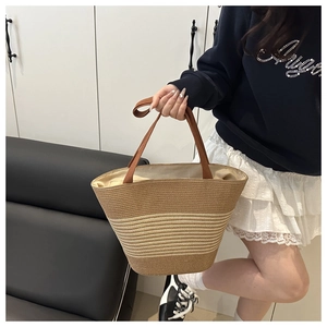 Detail of bohemian straw tote bag featuring striped woven texture and brown handles