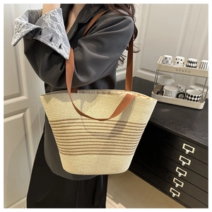 Detail of hand-woven straw bucket bag with brown stripes and crossbody strap on model