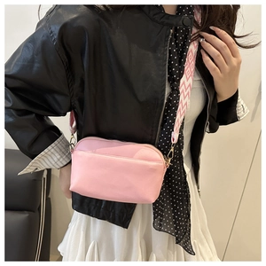 Detail of pink crossbody camera bag featuring a wide geometric pattern woven strap