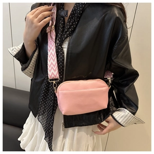 Détail du sac bandoulière rose avec une large bandoulière décorative à motif ondulé
