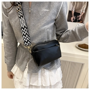 Detail of minimalist black crossbody bag with wide geometric woven shoulder strap and gold hardware