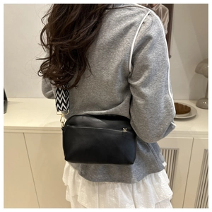 Sac bandoulière noir chic avec large sangle à chevrons portée à l'épaule par le modèle