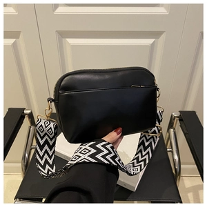 Detail of black leather crossbody bag with geometric woven wide strap and gold hardware