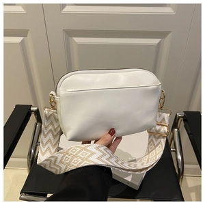 Close-up of white crossbody bag featuring wide geometric woven strap and gold hardware