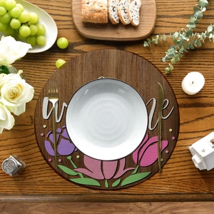 Detail of round linen placemat with tulip floral print and Welcome text on dark wood