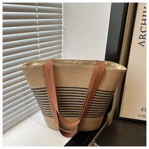 Detail of a large straw tote bag featuring black stripes and brown woven shoulder straps