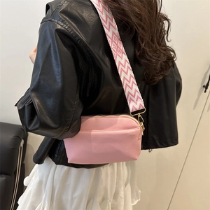 Sac bandoulière rose chic avec large sangle à motifs et garniture dorée sur une veste en cuir