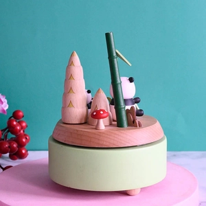 Handcrafted wooden panda music box with bamboo forest scene on a pink display stand