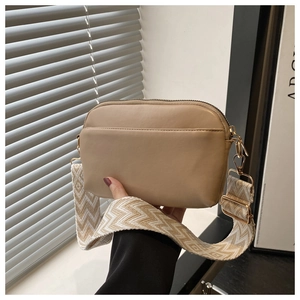 Close-up of khaki square crossbody bag with wide woven strap and golden hardware details