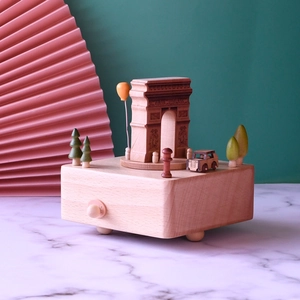Wooden Arc de Triomphe music box with miniature trees and cars on a marble surface