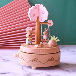 Wooden music box with rabbit on swing under cherry blossom tree, mechanical gift