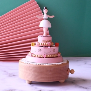 Detail of wooden ballerina music box featuring pink birthday cake layers and a wind-up knob