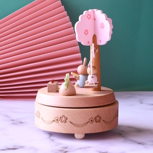 Close-up of wooden music box showing a pink cherry tree and rabbits on marble surface