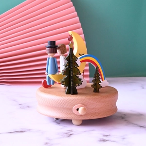 Rainbow wooden music box with moon and couple figures on a polished marble surface