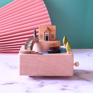 Detail of wooden music box featuring a miniature bridge and house on white marble