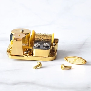 Golden 18-note mechanical music box movement with winding key on marble background