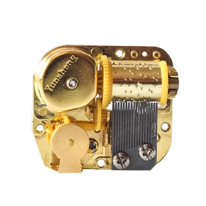 Golden mechanical wind-up music box movement with precision gears on white background