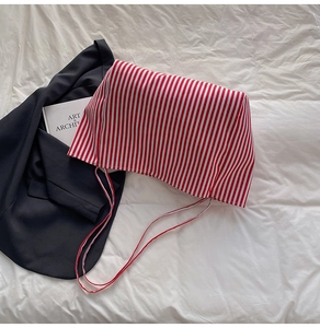 Detail of red and white striped tote bag with thin drawstring on a textured surface