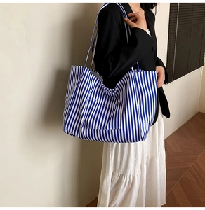 Close-up of blue and white striped canvas tote bag worn by a model in a minimalist room