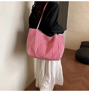 Detail of red and white striped canvas tote bag with front pocket shown on model shoulder