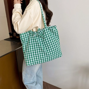 Green and white plaid canvas tote bag with a bow tie strap shown on shoulder