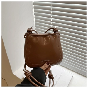Detail of a dark brown PU leather bucket bag with silver lettering and knotted strap