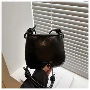 Detail of black faux leather mini bag featuring silver lettering and knotted strap