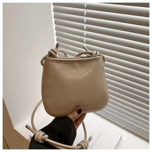 Detail of minimalist apricot crossbody bag featuring embossed text and rope shoulder strap