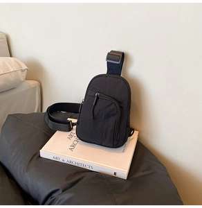 Minimalist black nylon crossbody bag placed on white books for a stylish lifestyle detail