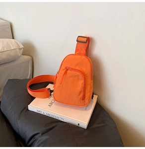 Detail view of an orange nylon chest bag on a book with a zipper and adjustable strap
