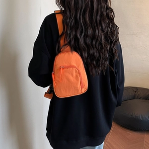 Bright orange nylon mini chest bag with adjustable black strap worn over a black hoodie
